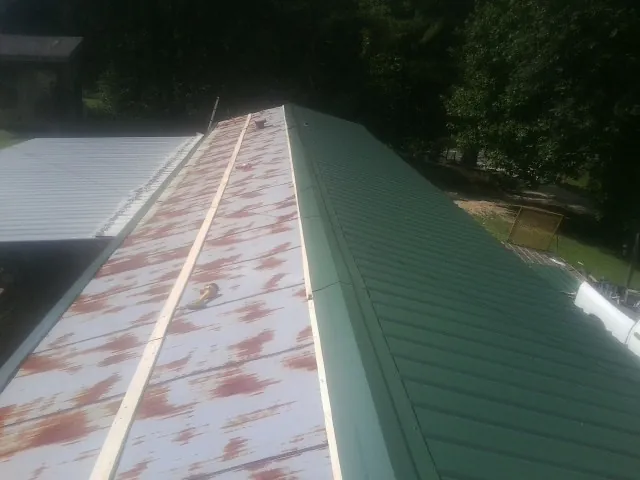 Old rusted panels beside newly installed green metal roofing — Wind Damage Roof Repair by Roofing Brothers in Creighton